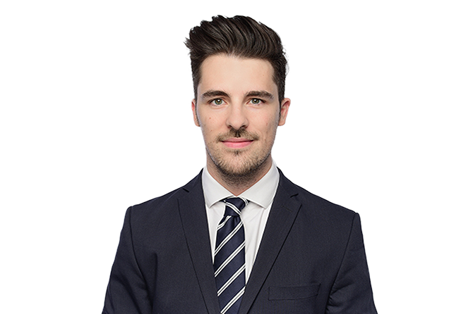 The image shows a person wearing a dark suit with a striped tie against a black background.