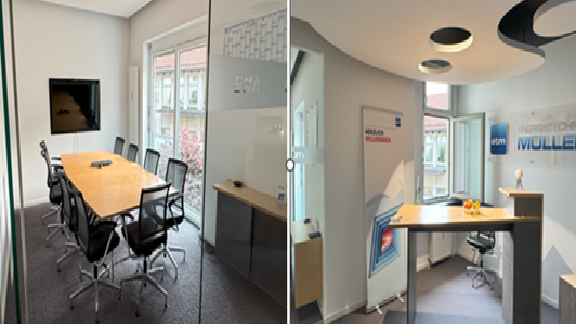 The image shows two interior spaces: one is a conference room with a long table surrounded by office chairs and a large screen on the wall, and the other is a reception area with a desk, signage, and marketing materials. Both areas have windows allowing natural light to enter.